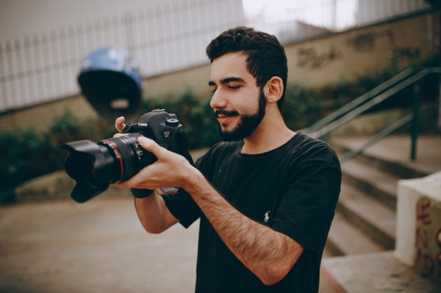 Chlapec v čiernom tričku stojí pri schodoch a fotografuje s veľkým fotoaparátom